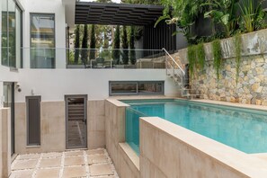 Ein moderner Poolbereich im Freien mit einer Steinwand, einer Glastrennwand und einer Pergola.