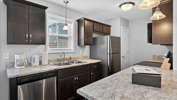 A modern kitchen with dark wood cabinets, stainless steel appliances, a granite countertop, and pendant lighting. - Cozy 2br Stay Near Work & Dining (Clarksville)