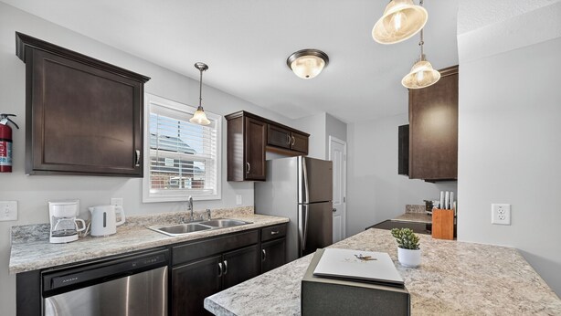 A modern kitchen with dark cabinets, stainless steel appliances, a granite countertop, and pendant lighting. - Bright, Modern 2 bedroom Home Away From Home (Clarksville)