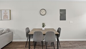 A dining area with a wooden table, four grey chairs, a clock, a small potted plant, and a grey sofa. - Bright, Modern 2 bedroom Home Away From Home (Clarksville)