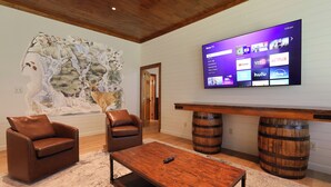 A living room with a mounted TV, leather chairs, a coffee table, and a rustic wooden bench. - Pool table, hot tub, indoor sauna, outdoor spaces, big kitchen in Gatlinburg! (Gatlinburg)