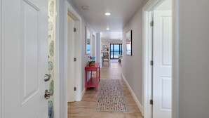 A hallway with white doors, a patterned rug, and a red table with a vase. - Sea Oats 117 | 2BR/2BA Boca Grande Gulf Front Luxe (Boca Grande)