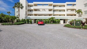 A multi-story hotel with a central courtyard, palm trees, and a red car parked in front. - Sea Oats 117 | 2BR/2BA Boca Grande Gulf Front Luxe (Boca Grande)