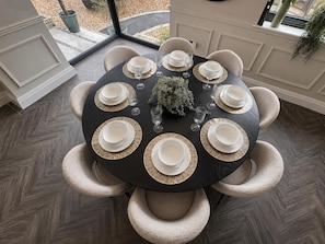 A round dining table with white plates and gold accents, surrounded by beige chairs, set for six.