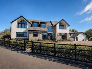 A modern two-story house with a stone facade, large windows, and a fenced driveway.