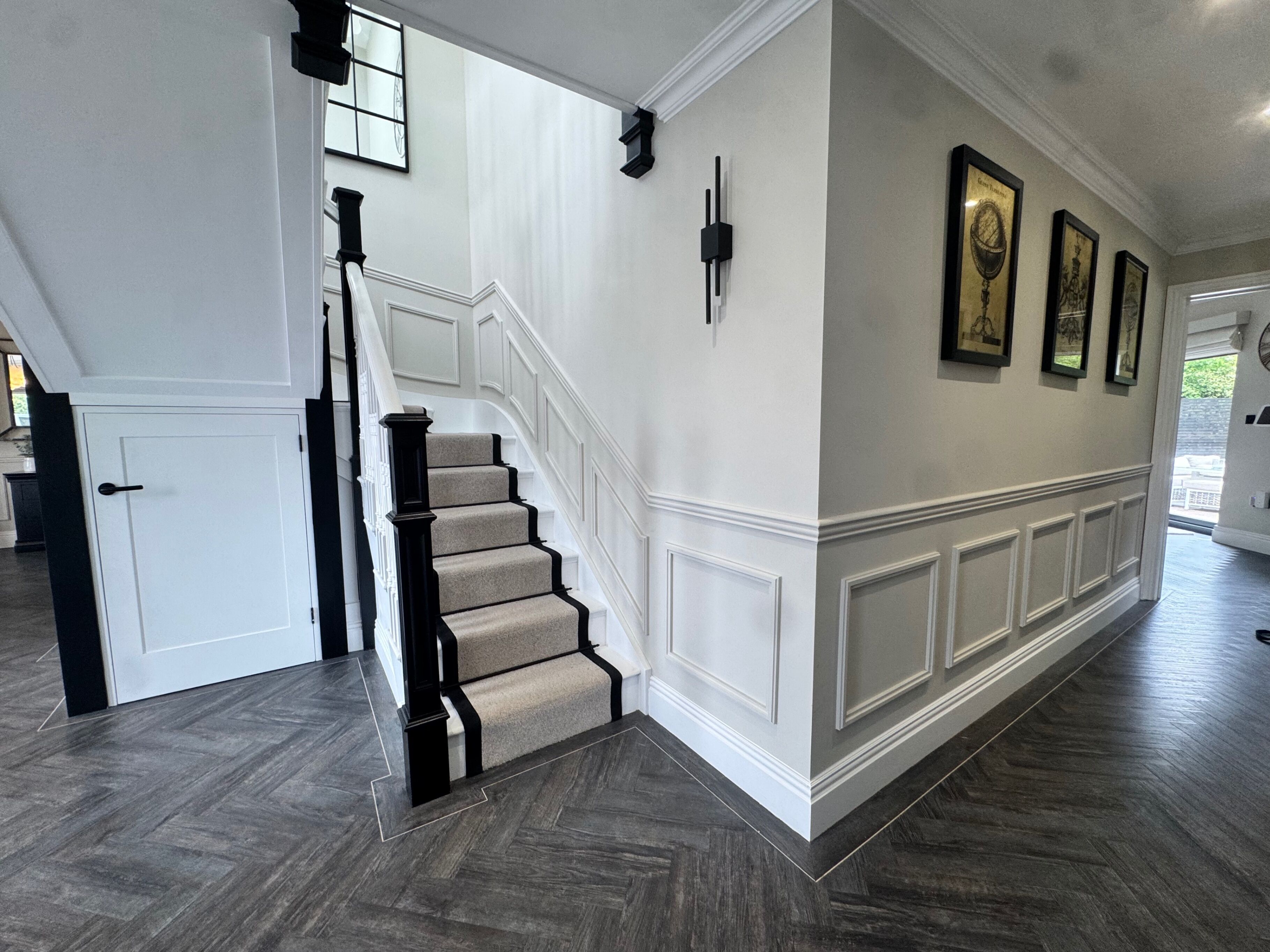Un escalier avec des marches en bois foncé et une moquette beige, menant à une porte blanche dotée d’une poignée noire.