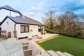 Ein modernes Haus mit Terrasse, Rasen und Holzterrasse.
