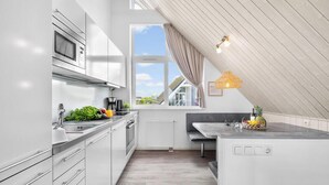 Eine moderne Küche mit weißen Schränken, einer eingebauten Mikrowelle und einem Fenster mit Außenblick.