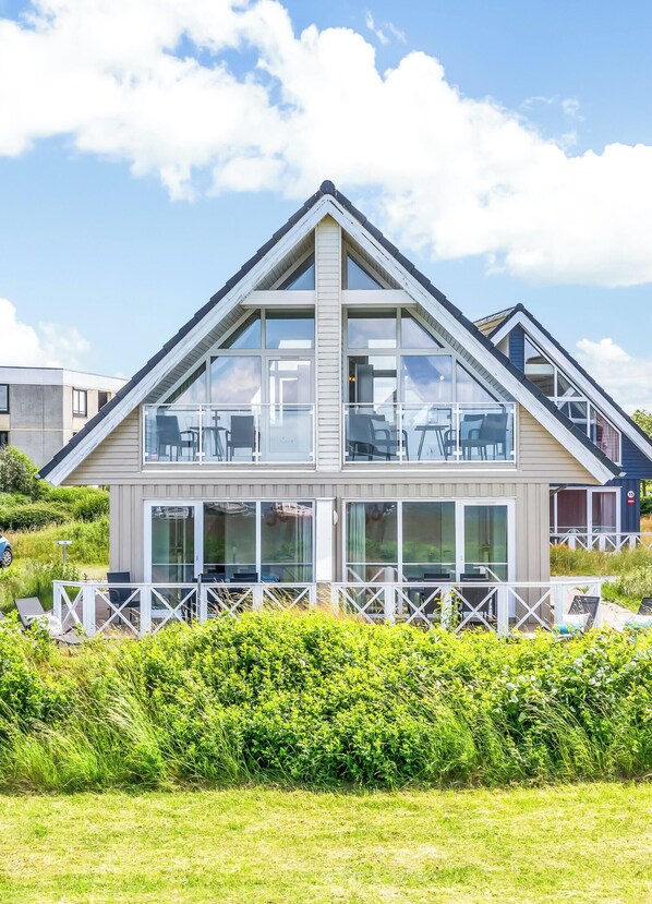 Ein modernes, zweistöckiges Haus mit großen Fenstern, einem Balkon und einem weißen Zaun.