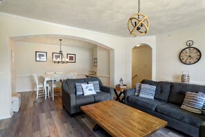 A living room with a sofa, coffee table, dining area, and a clock on the wall.