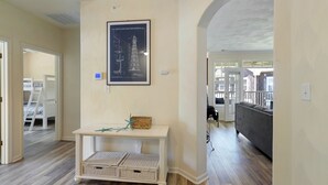 Ett vardagsrum med ett vitt konsolbord, korgar av rotting, en inramad arkitektonisk ritning och en grå soffa.