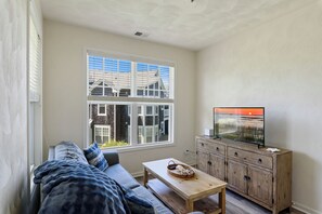 Una sala de estar con un sofá, una mesa de madera, un televisor y una ventana con persianas.
