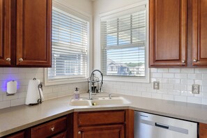 A kitchen with wooden cabinets, a white countertop, a sink, and a window with blinds.