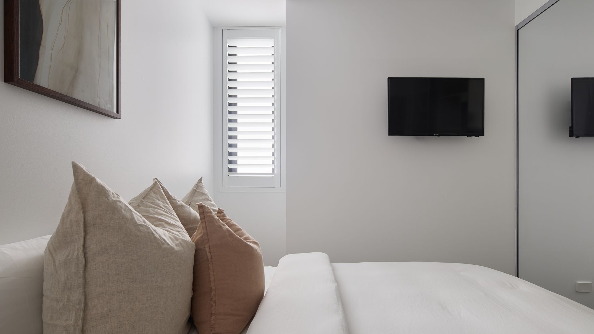 A bedroom with a bed, pillows, a window with blinds, a TV, and a door.