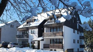Un immeuble à plusieurs étages doté de balcons, d’un espace de stationnement et entouré d’un paysage enneigé.
