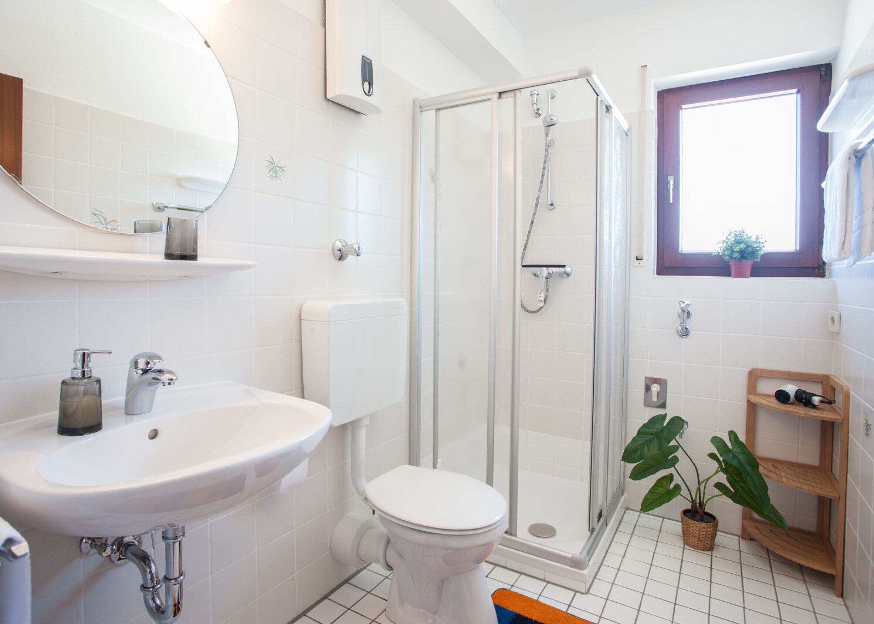 A modern bathroom with a glass-enclosed shower, a white toilet, a sink with a mirror, and a small window with a plant.