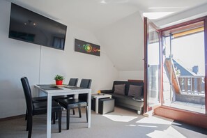 Una sala de estar moderna con comedor, televisor de pantalla plana, un cuadro y un amplio ventanal con vistas.