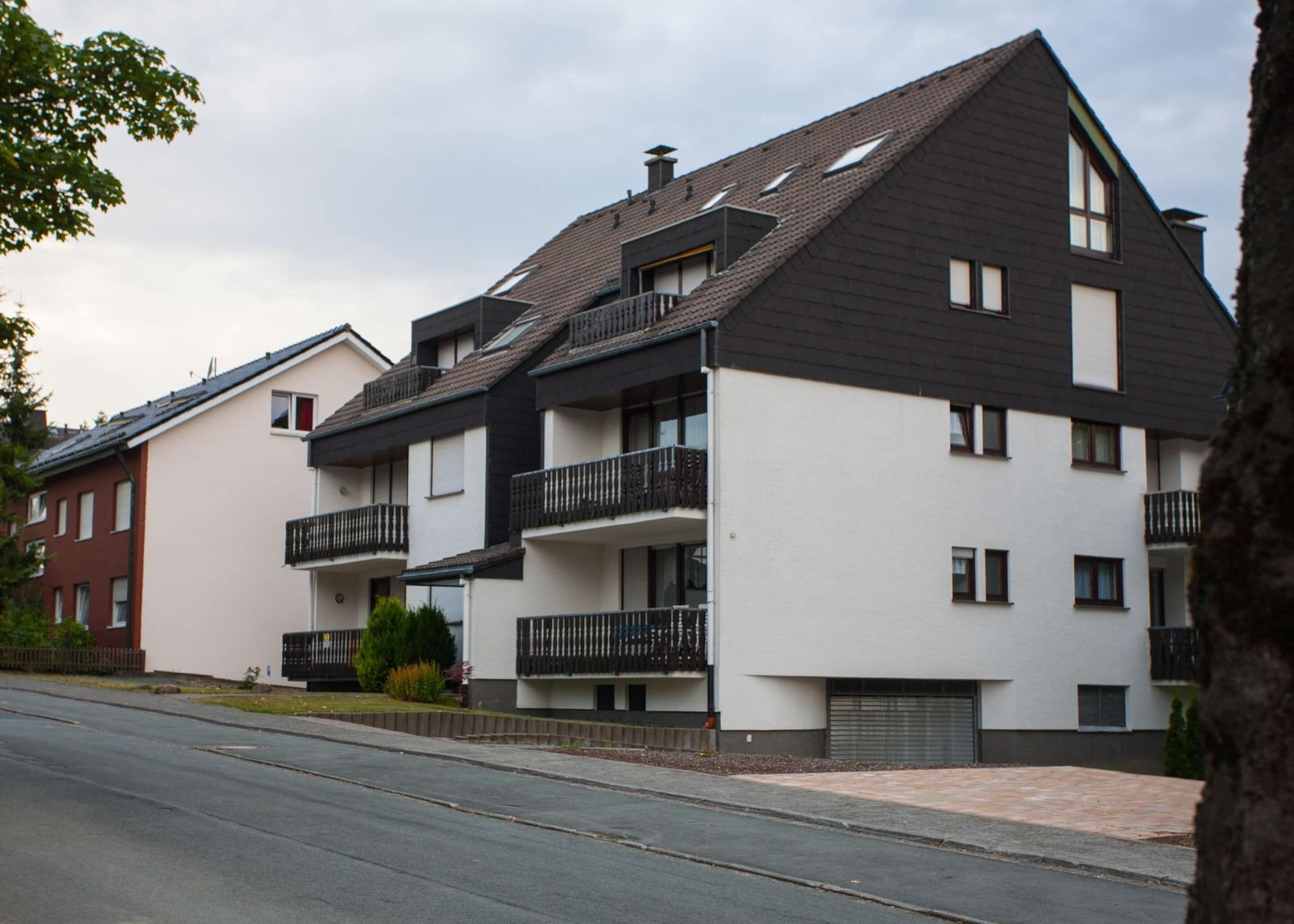 A modern multi-story residential building with balconies, a flat roof, and a paved driveway.