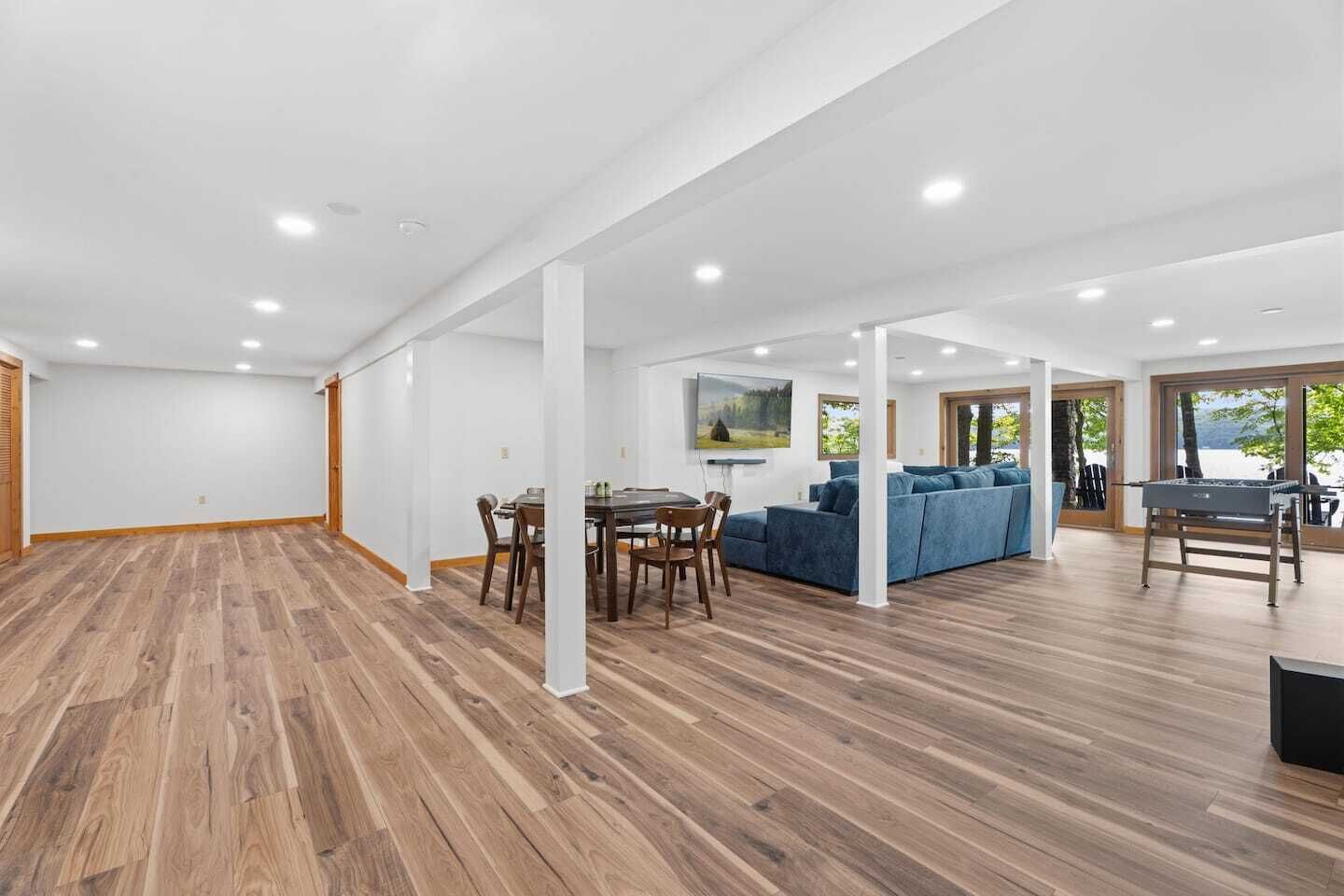Une pièce spacieuse avec un plancher en bois, un coin repas comprenant des chaises et une table, un canapé bleu et un barbecue.