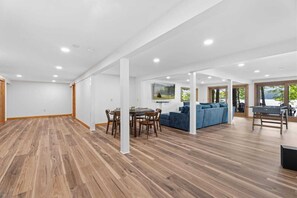 Een ruime kamer met houten vloeren, een zithoek met stoelen en een tafel, een blauwe bank en een grill.