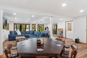 Een moderne woonkamer met een grote blauwe bank, een houten eettafel met stoelen en een tafelvoetbaltafel.