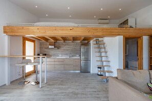 Een moderne keuken met een centraal eiland, een eethoek met tafel en stoelen, en een slaapgedeelte met een houten plafond.