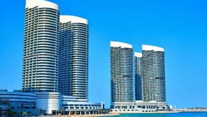 Un hotel frente al agua con tres edificios altos cilíndricos, un puerto deportivo y un cielo azul despejado.