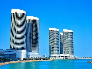 Ein Hotel am Wasser mit drei zylindrischen Hochhäusern, einem Jachthafen und einem wolkenlosen, blauen Himmel.