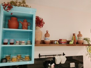 Cuina amb un armari blau que conté ceràmica i tasses, una estantalia amb objectes decoratius i utensilis de cuina penjats.