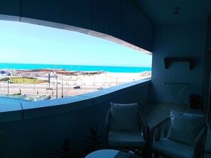 Una habitación con ventanal curvo que da a una playa y un estacionamiento.