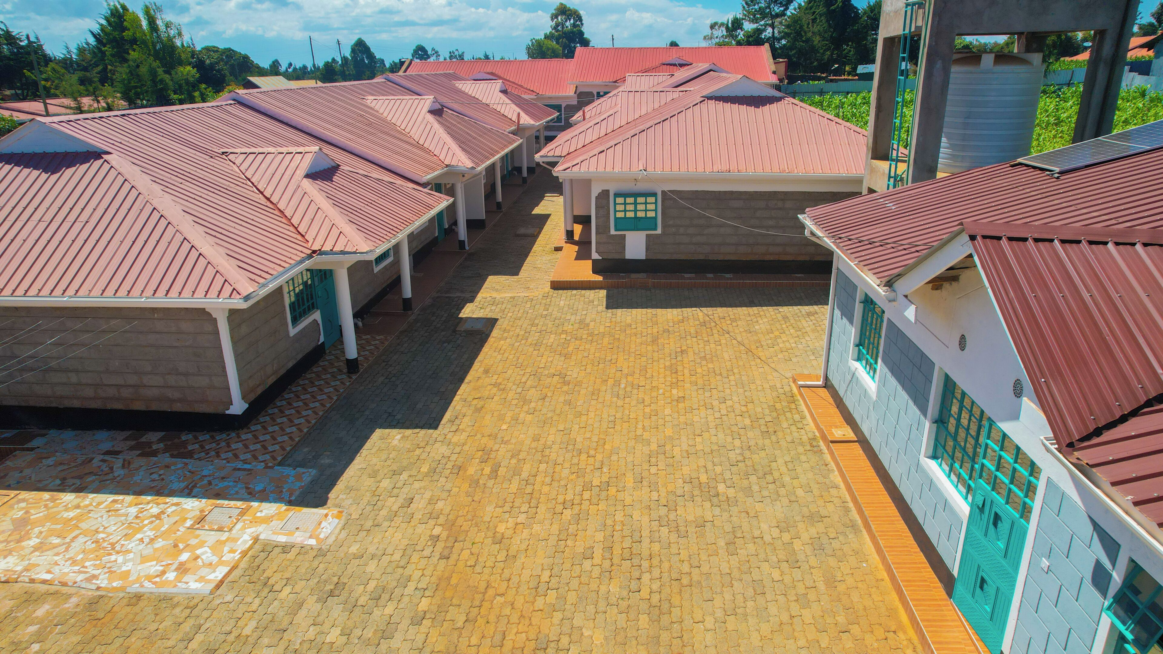 A row of small, single-story buildings with red roofs, arranged in a linear fashion on a paved ground.
