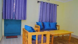 Une pièce avec une porte bleue, une table en bois, deux chaises et des rideaux violets.