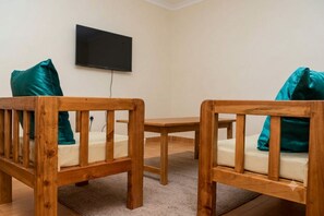 A room with two wooden chairs with cushions, a small table, and a mounted television on the wall.