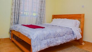 Un lit simple avec un cadre en bois et une couvre-lit à motifs floraux, une fenêtre avec des rideaux à motifs et un mur uni.