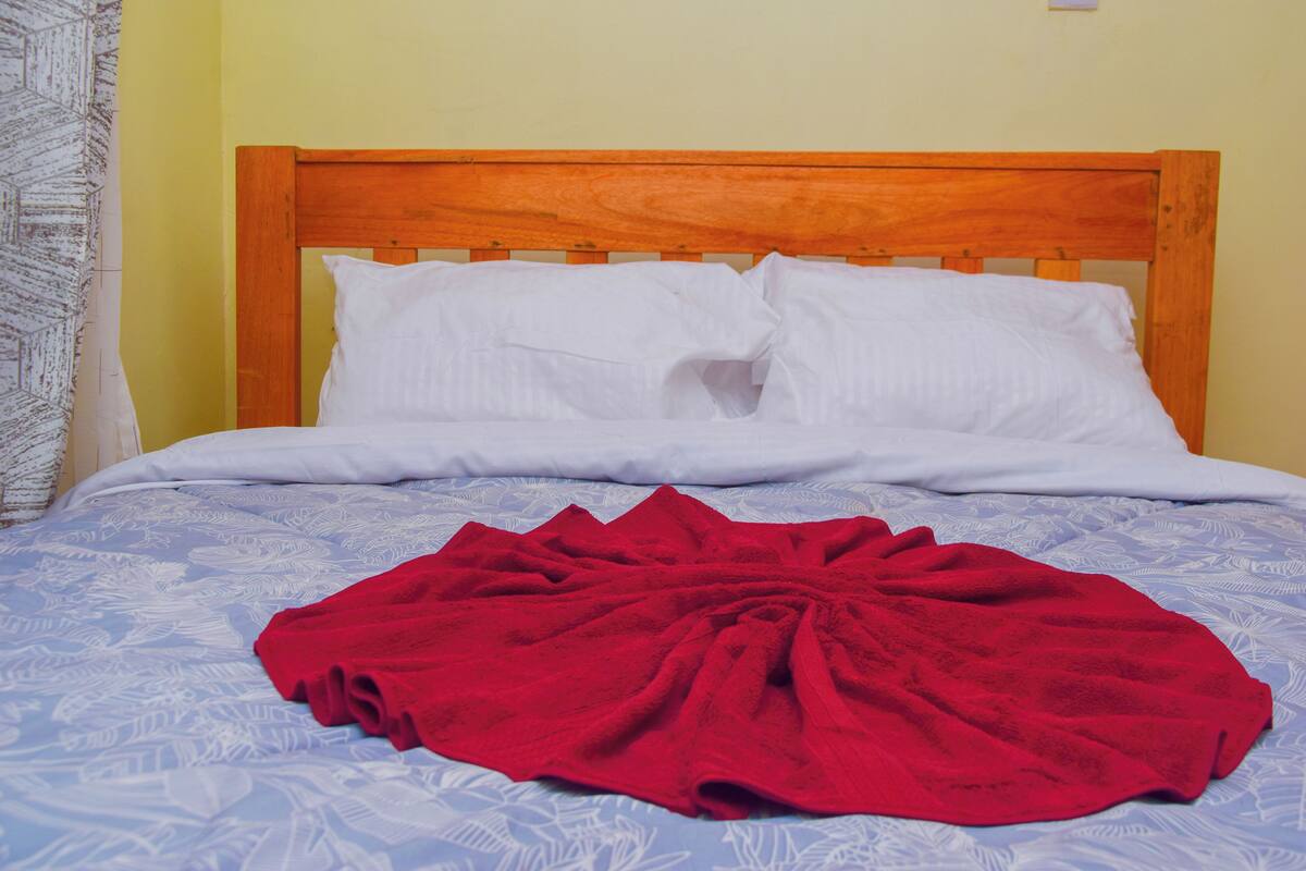 A bed with a wooden headboard, white pillows, and a red blanket.