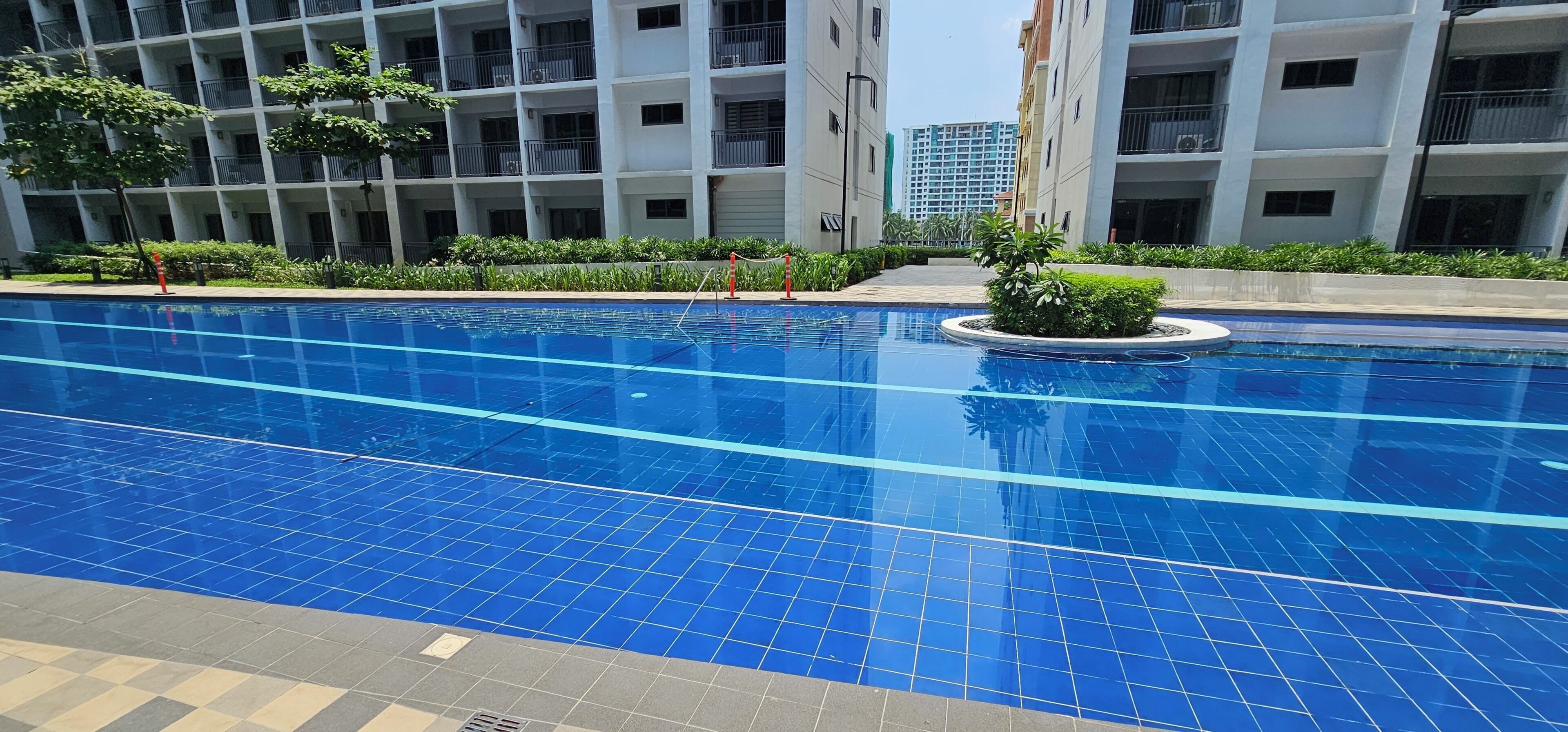 Una piscina con piastrelle blu, circondata dal verde e da edifici moderni.