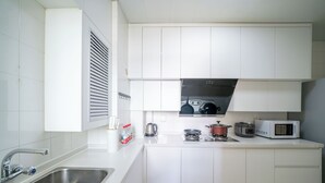 A modern kitchen with white cabinets, stainless steel sink, microwave, and a gas stove. - Tyms 2BR 1BA Family Serviced Residence (Shanghai)