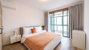 A modern hotel room with a large bed, a nightstand, a desk, and a window with curtains. - Tyms 2BR 1BA Family Serviced Residence (Shanghai)