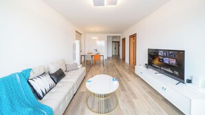 A modern living room with a sofa, coffee table, TV, and a dining area with chairs and a table. - Tyms 2BR 1BA Family Serviced Residence (Shanghai)