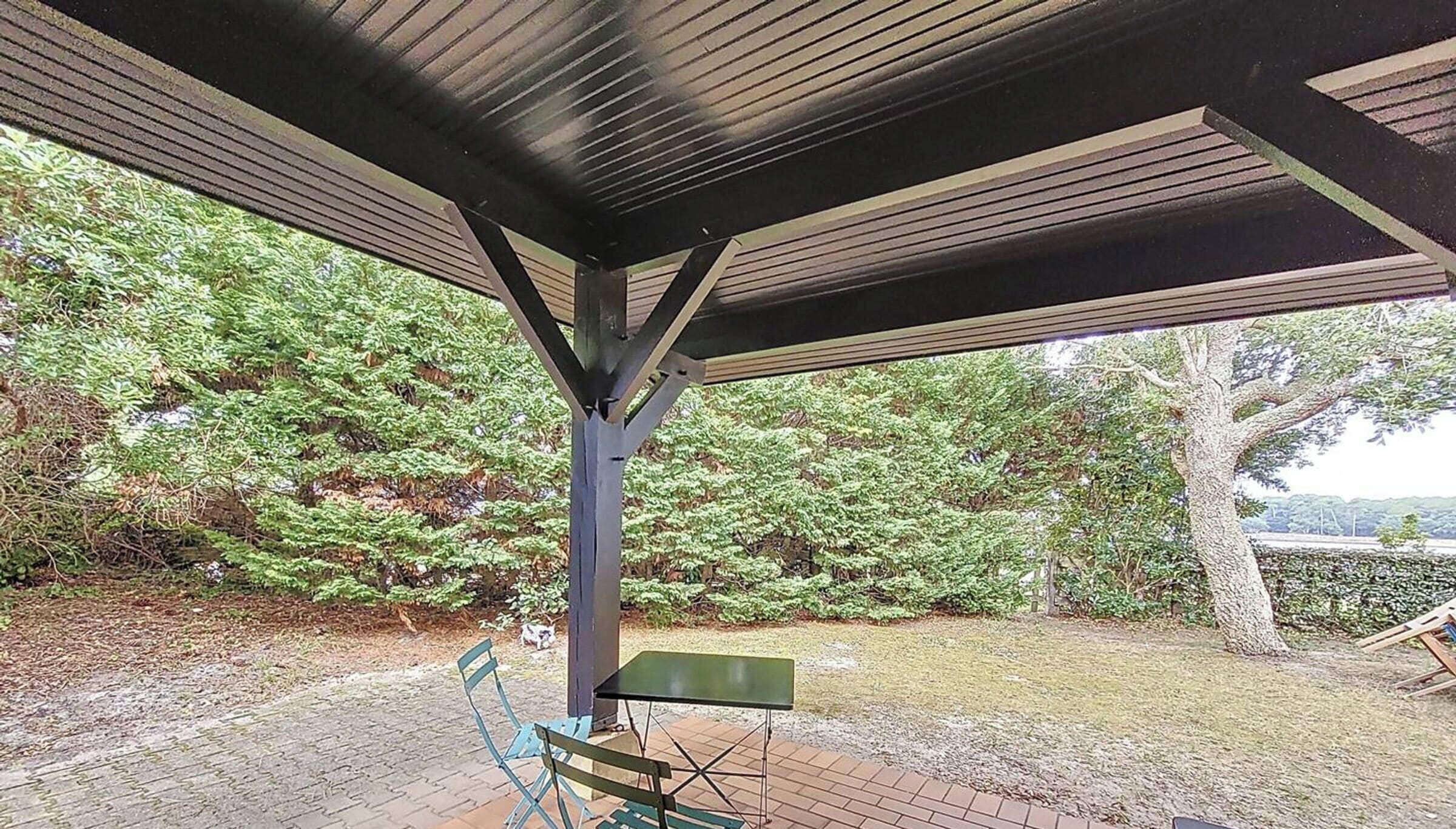 Un espacio al aire libre techado con piso de ladrillo, una mesa de metal y un banco.