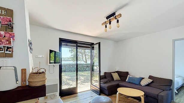 A modern living room with a sofa, ottomans, a small table, a TV, and a sliding glass door leading to an outdoor area. - Villa lake view, pets welcome - 6 guests (Soustons)