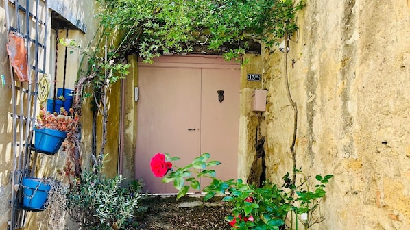 Une ruelle étroite avec une porte rose, des jardinières bleues suspendues et une fleur rouge.