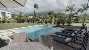 A pool area with a rectangular pool, lounge chairs, a round wicker table, and a covered umbrella. - All inclusive paid at the resort  (Puerto Plata)