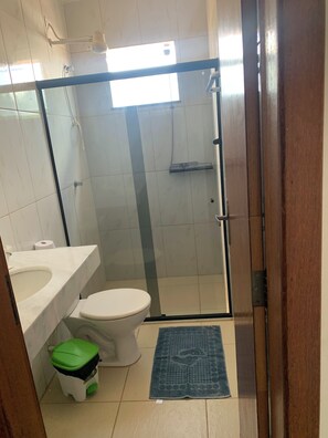 Casa de banho com sanita, lavatório, chuveiro e um pequeno contentor de lixo.