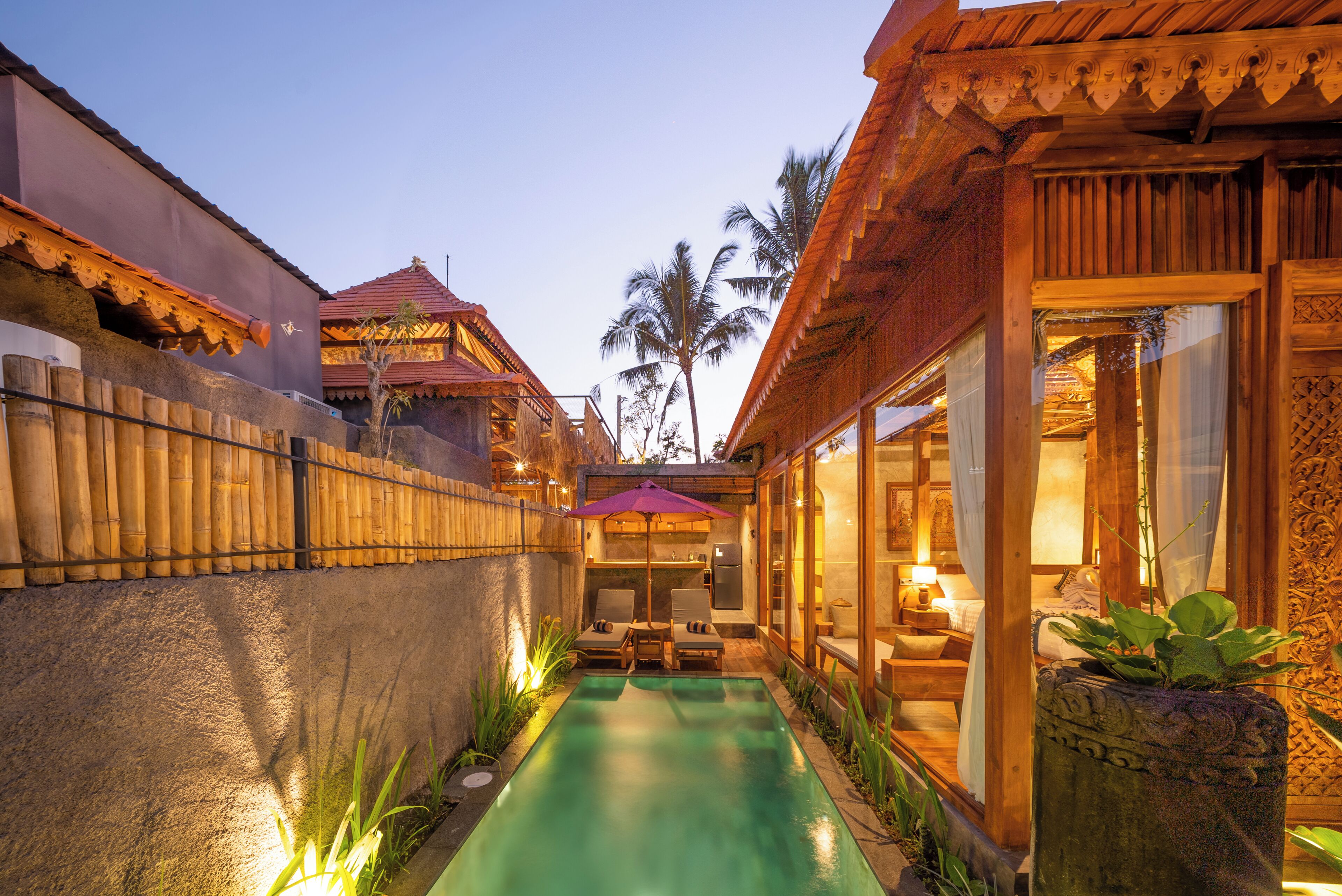 A pool with lounge chairs, a wooden fence, and a building with a red roof.