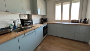 Eine moderne Küche mit grauen Schränken, einer Holzauskładung, einem eingebauten Ofen und einem Fenster mit Jalousien.