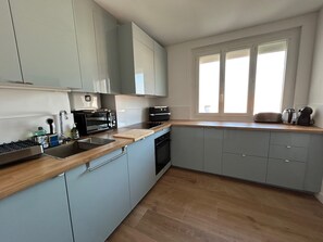 Eine moderne Küche mit grauen Schränken, einer Holzauskładung, einem eingebauten Ofen und einem Fenster mit Jalousien.