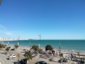 Eine Küstenstraße mit parkenden Autos, Fahrrädern und freiem Blick auf das Meer.
