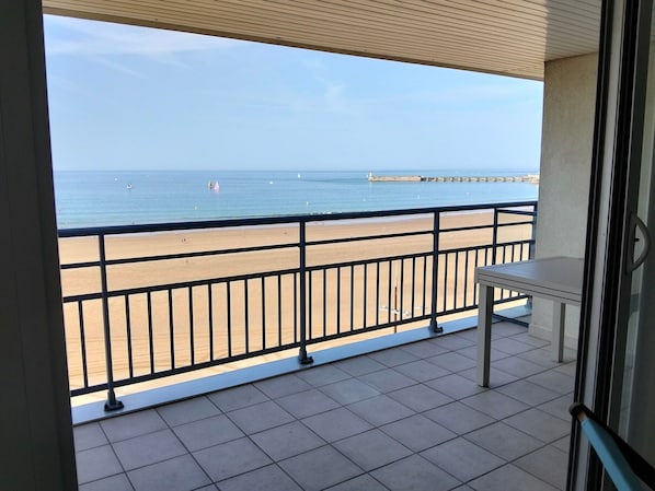A balcony with a view of a beach, a tiled floor, and a table. - Beautiful apartment with sea view - 4 guests (Les Sables-d'Olonne)