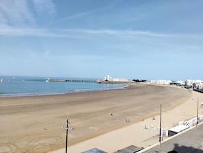 A wide sandy beach with a clear sky, a pier extending into the water, and buildings in the background. - Beautiful apartment with sea view - 4 guests (Les Sables-d'Olonne)